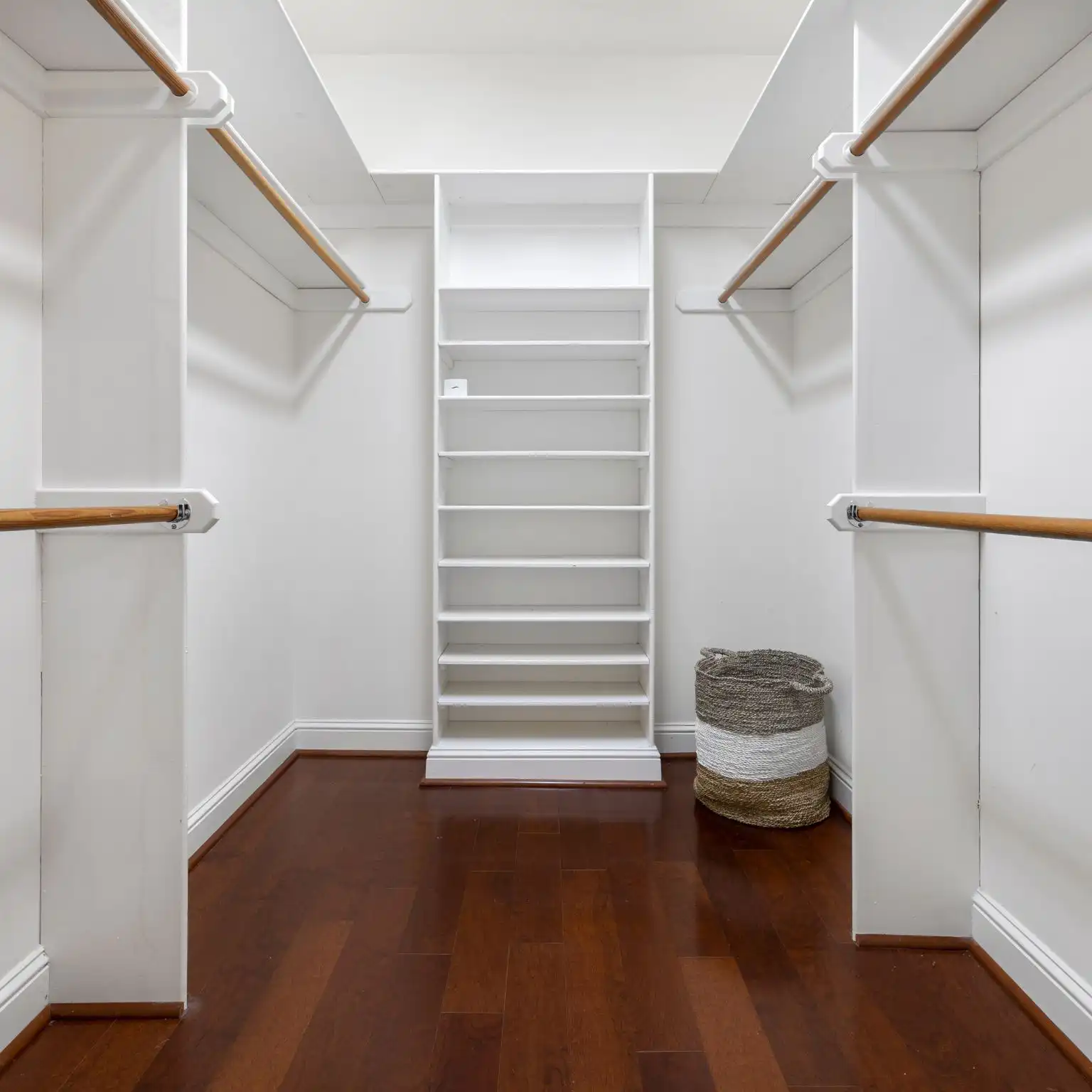 Custom closet design featuring open shelving, wooden hanging rods, and a woven storage basket, showcasing tailored storage solutions for maximizing space in Cape Coral homes.